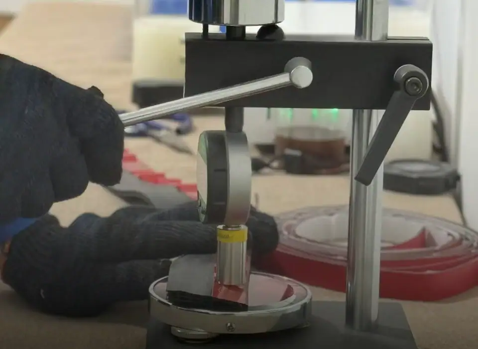 Laboratory material testing machine performing compression test on a sample with a mechanical press and digital measurement tools.