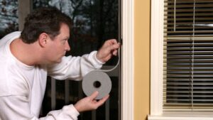 Man applying weather stripping to window to prevent air leakage and improve energy efficiency in a commercial building.